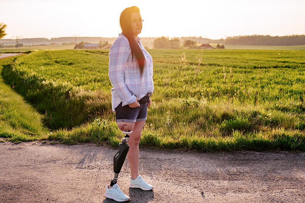 Eine Frau mit Endo-Exo Prothese steht in der Natur an einem Feld im Gegenlicht
