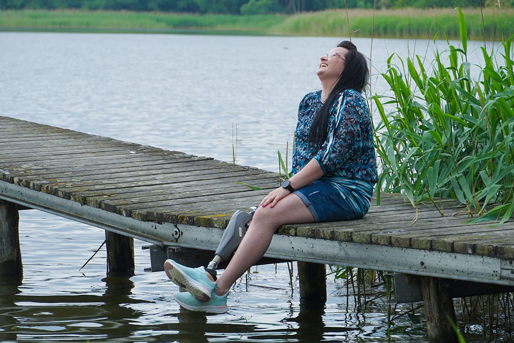 An endo-exo user sits laughing on a jetty and holds her feet above the water