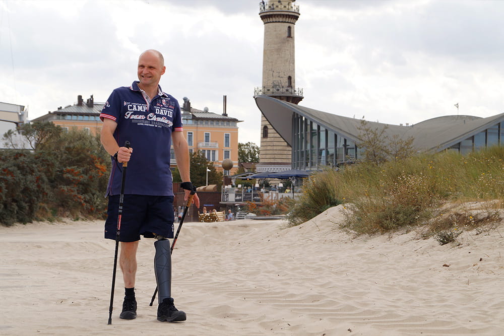 Ein Mann mit Beinprothese und Wanderstöckern am Strand