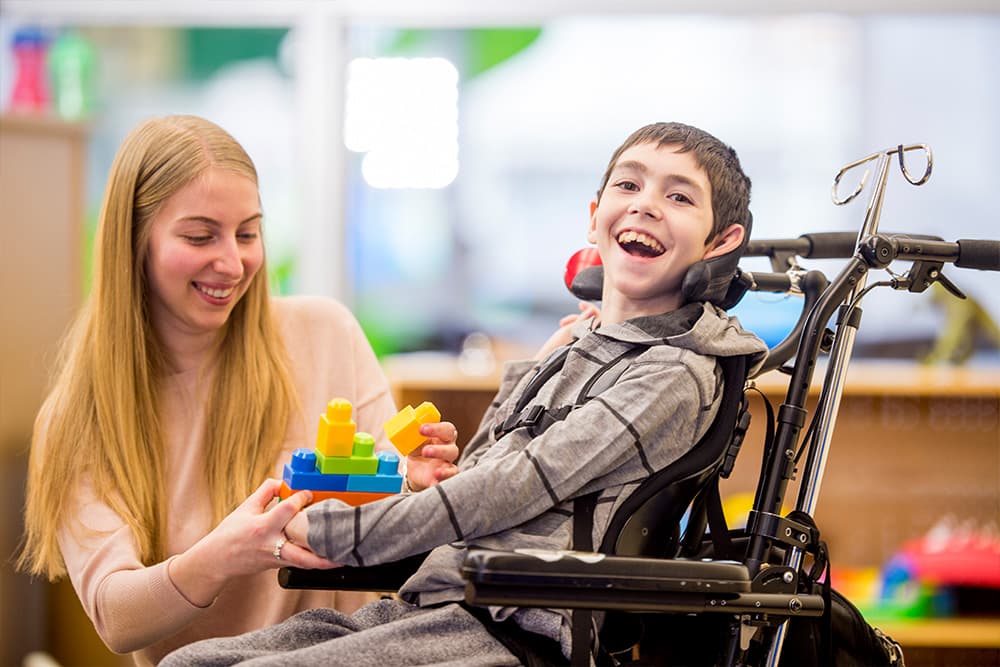 A child with a happy smile sits playing in a wheelchair