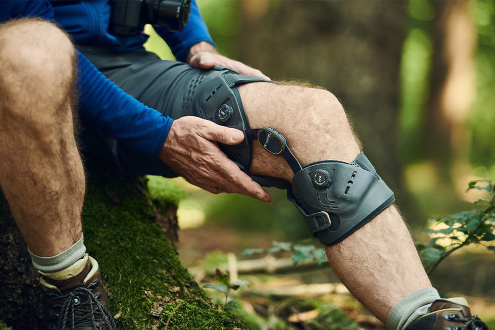 A man sits in the forest and wraps his hands around a leg orthosis