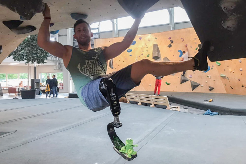 An athlete with a lower leg prosthesis hangs on the bouldering wall in an indoor climbing park.