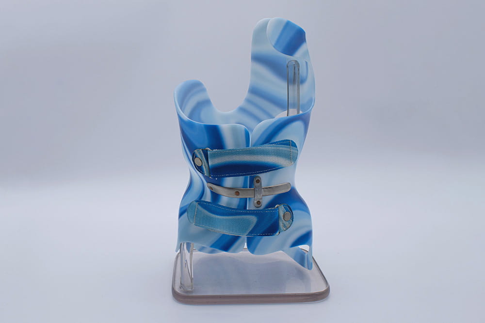 A trunk orthosis for very small people in blue on an acrylic stand