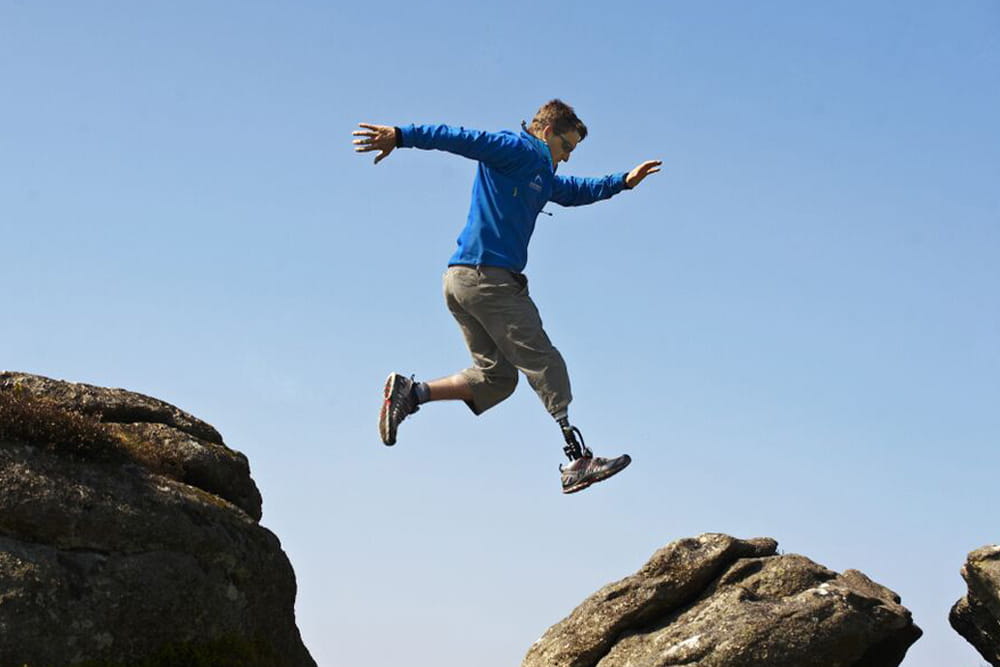 Ein Mann mit Prothese springt aktiv über Felsen