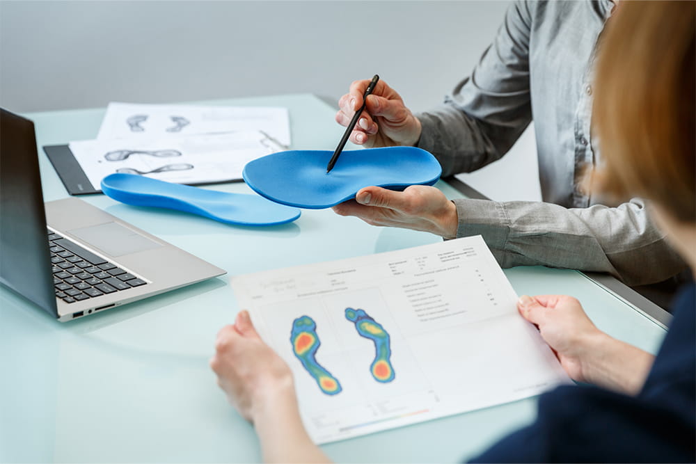 A man holds a blue insert in his hand and points to an area and a lady holds an evaluation of a foot measurement in her hand and looks at the man.