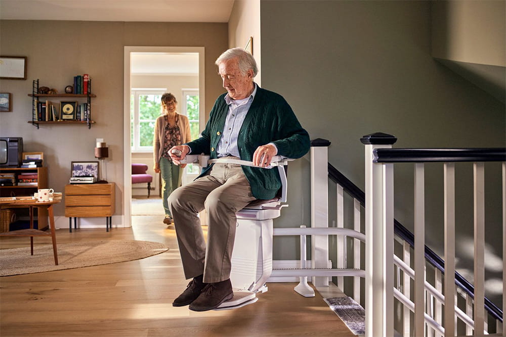 Ein Mann sitzt auf einem Treppenlift und steuert seine Fahrt mit einem Joystick.
