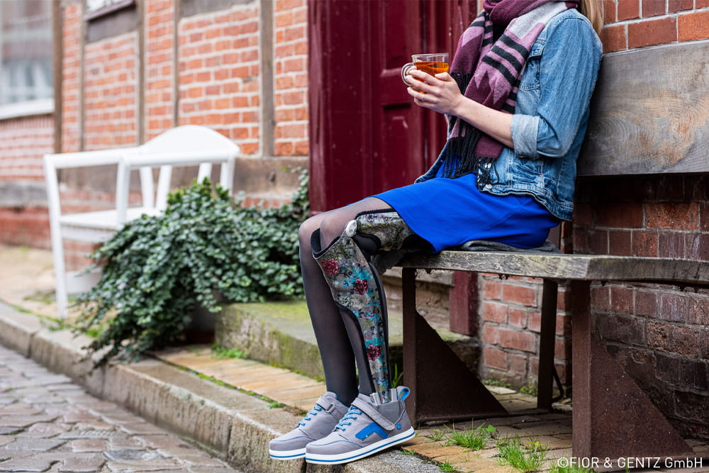 Eine Frau mit Ganzbeinorthese sitzt auf einer Bank und trinkt einen Tee.
