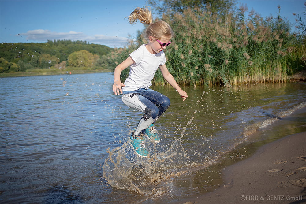 Ein Mädchen mit Beinorthese spielt im Wasser.