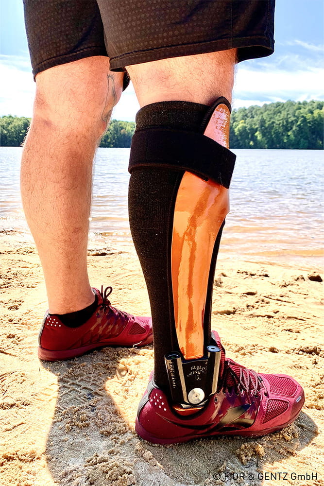 Ein Mann mit Beinorthese steht am Strand.