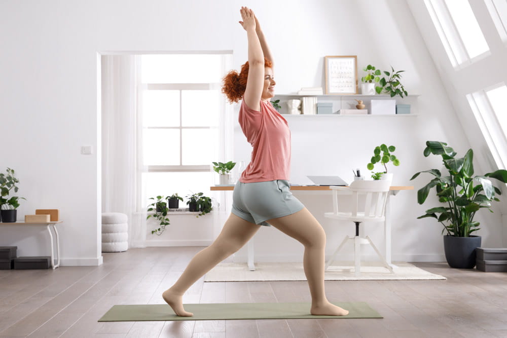 Eine Frau mit Kompressionsstrümpfen von medi macht Sport in der Wohnung.