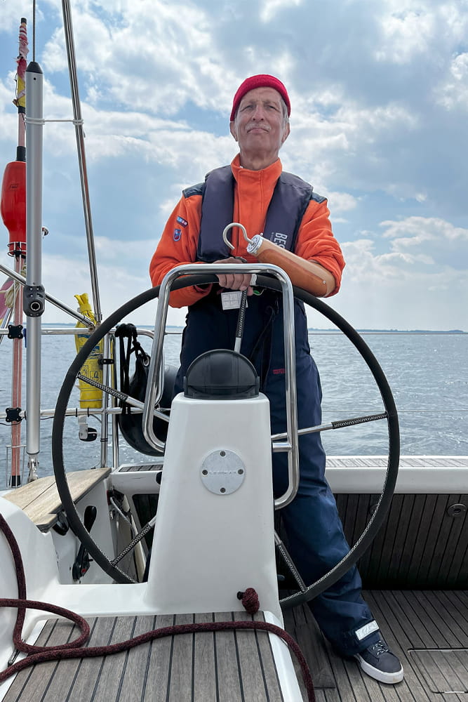 Ein Mann mit Armprothese und Greifhaken steht am Steuer eines Schiffes.