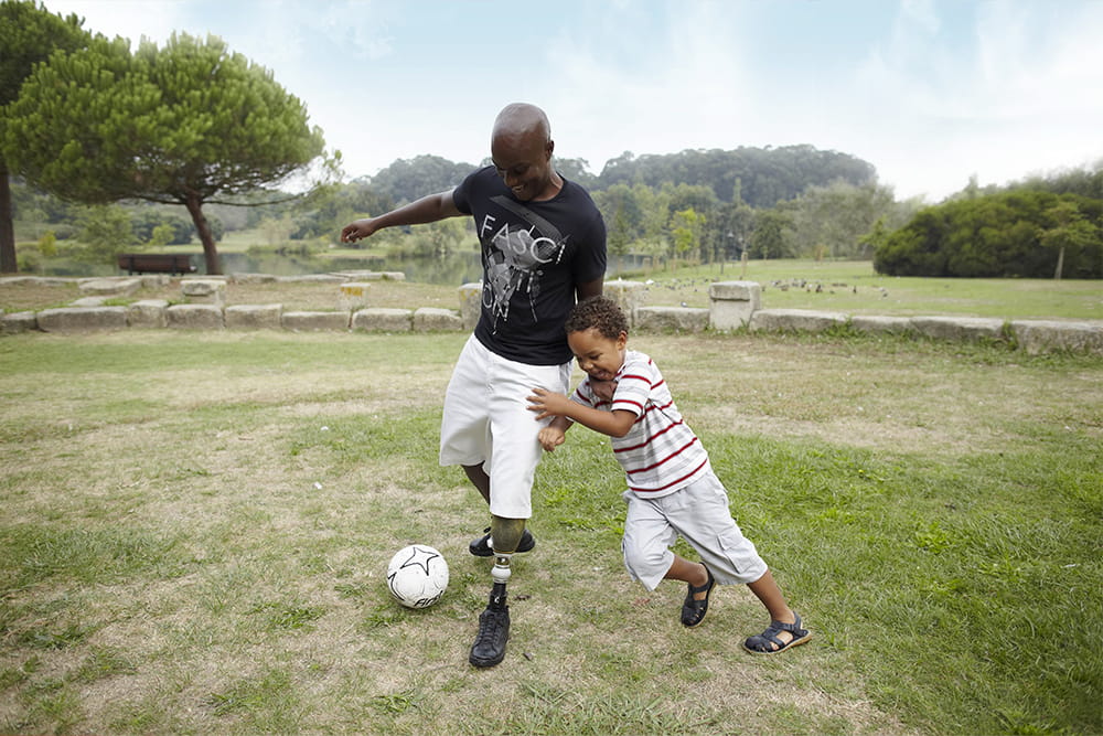 Ein Mann mit Beinprothese spielt Fußball mit seinem Sohn.