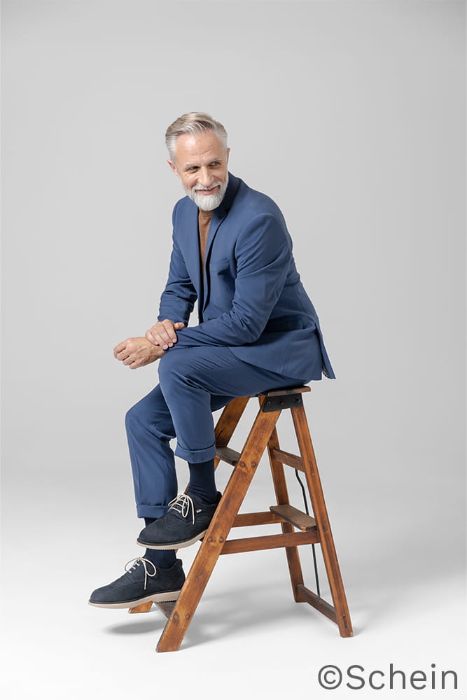 Ein Mann in Anzug sitzt auf einer kleinen tragbaren Leiter.